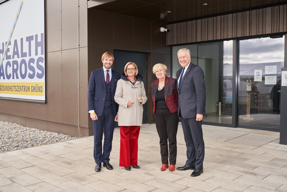 Vier Personen stehen vor dem Eingang des Gebäudes und lächeln.